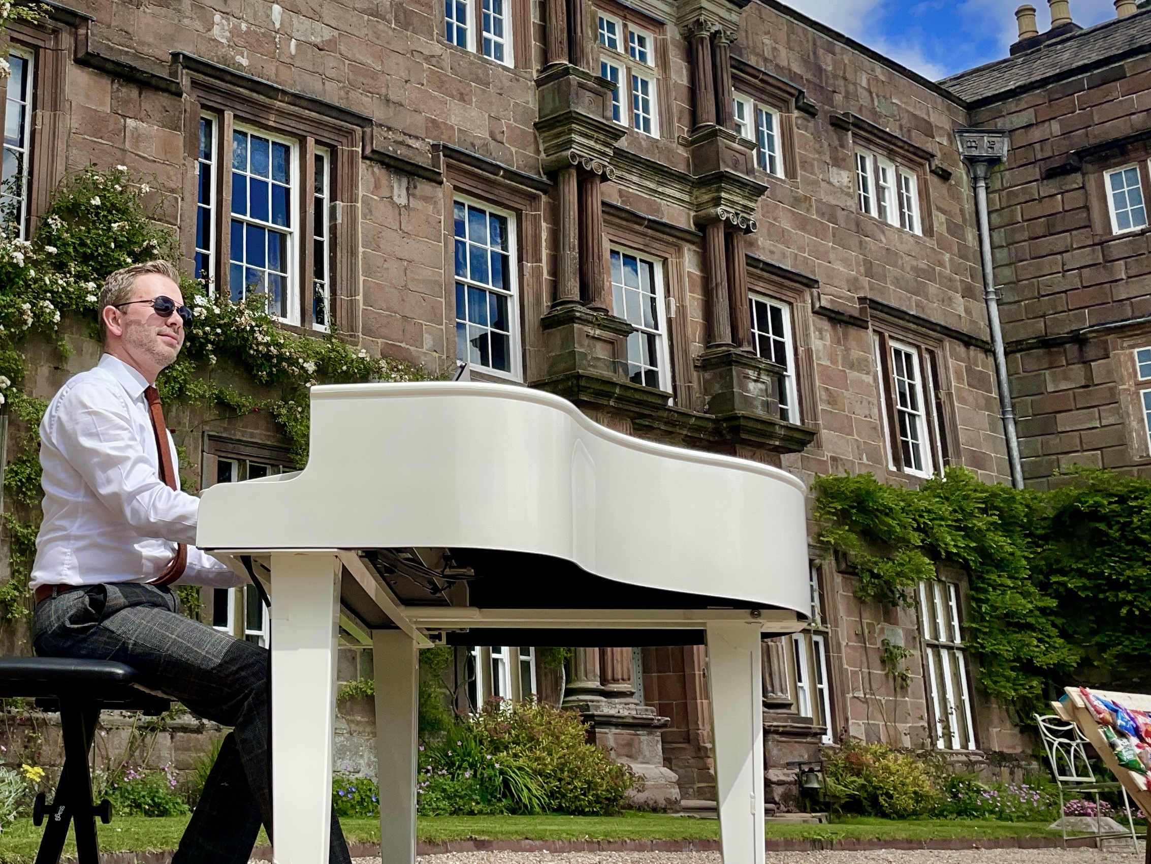 Wedding pianist Craig Smith playing his white piano during a Browsholme Hall outdoor wedding ceremony