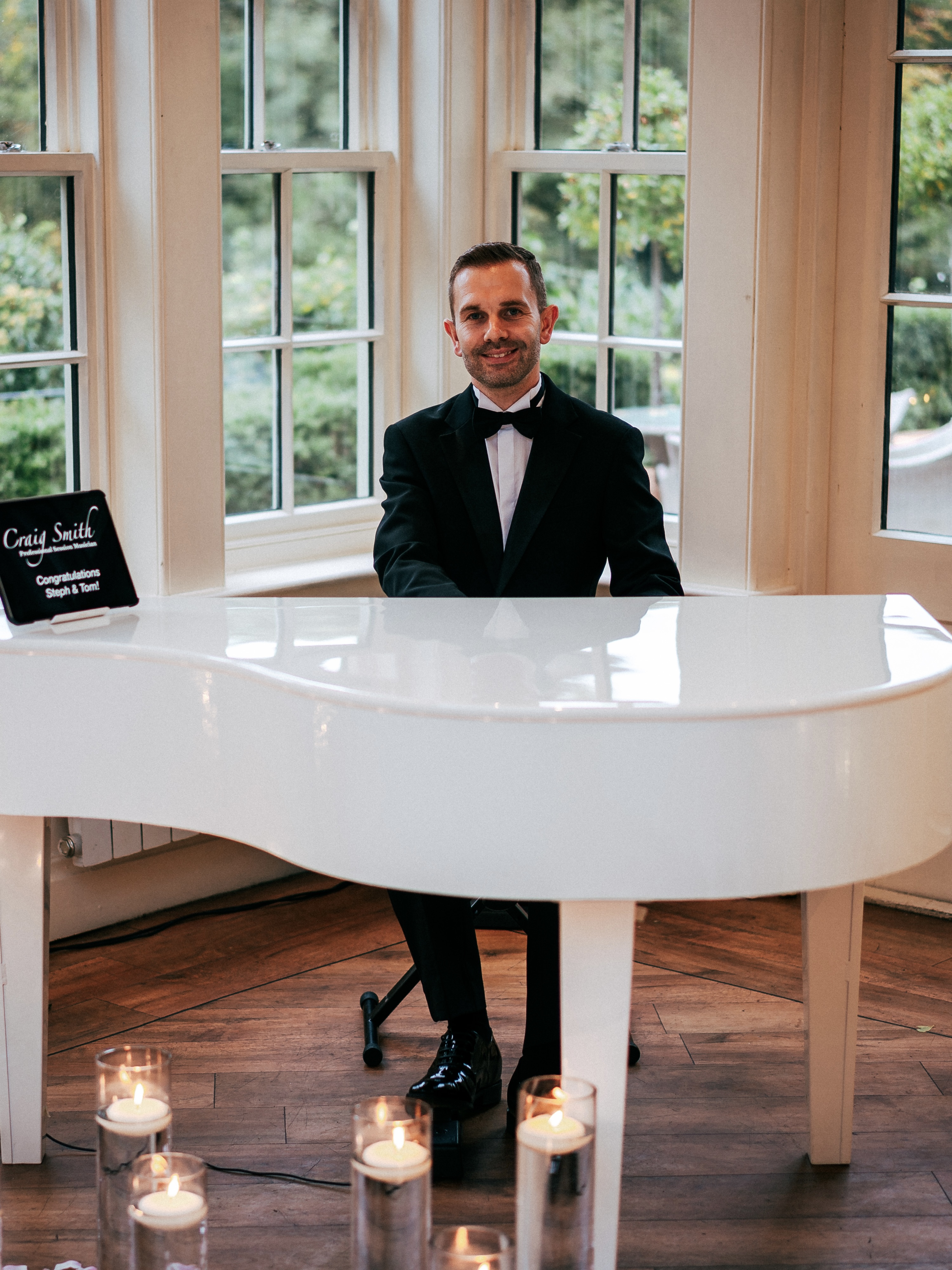 Craig Smith plays piano during a wedding breakfast at Mitton Hall, dressed in a black tuxedo.