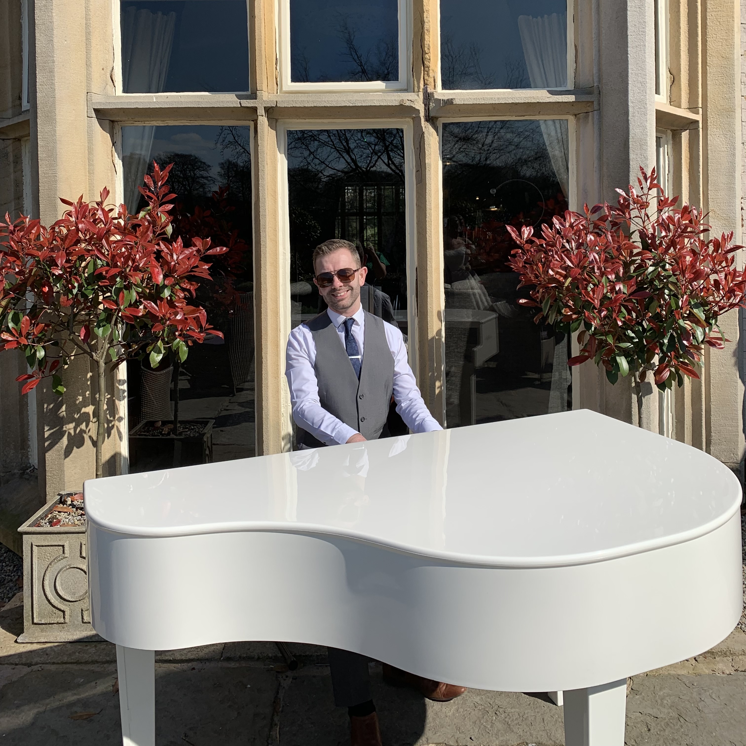 Mitton Hall wedding pianist Craig Smith performs on a white baby grand piano in the sunshine for a terrace drinks reception