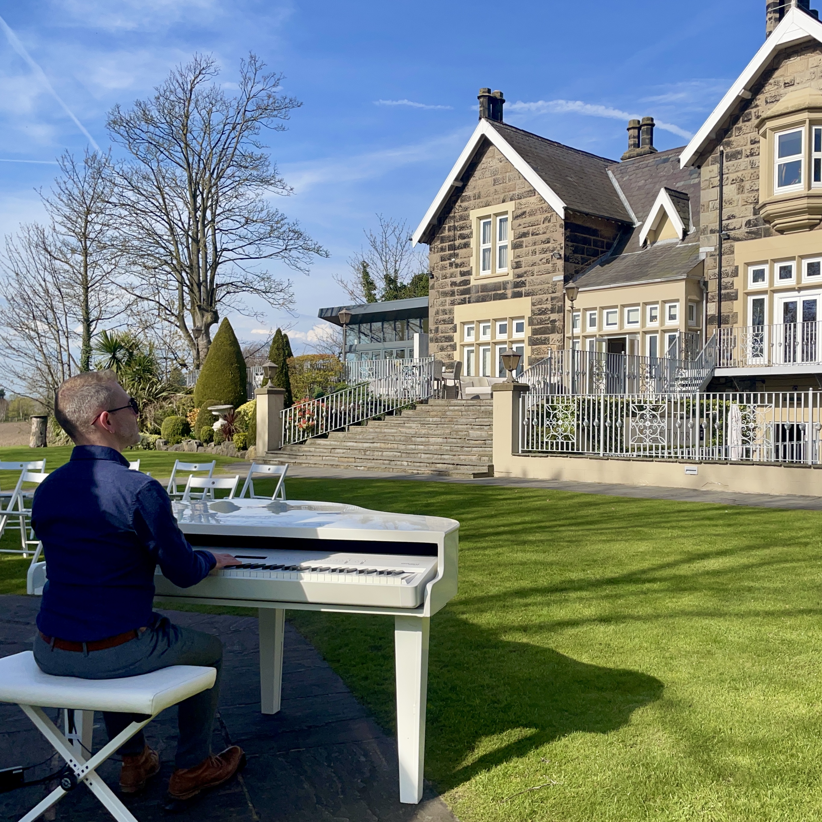 Pianist Craig Smith performs on a white baby grand positioned in the sunshine next to the wedding ceremony pagoda